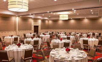 a large banquet hall with several round tables covered in white tablecloths and decorated with red flowers at Four Points by Sheraton Saginaw