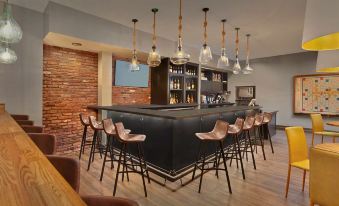 a modern bar with black counter , pendant lights , and wooden chairs under a brick wall at Scholar Morgantown, Tapestry Collection by Hilton