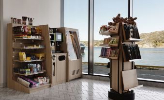 a coffee and food kiosk with shelves , including a drink dispenser and other products , in front of large windows at Scandic Havet