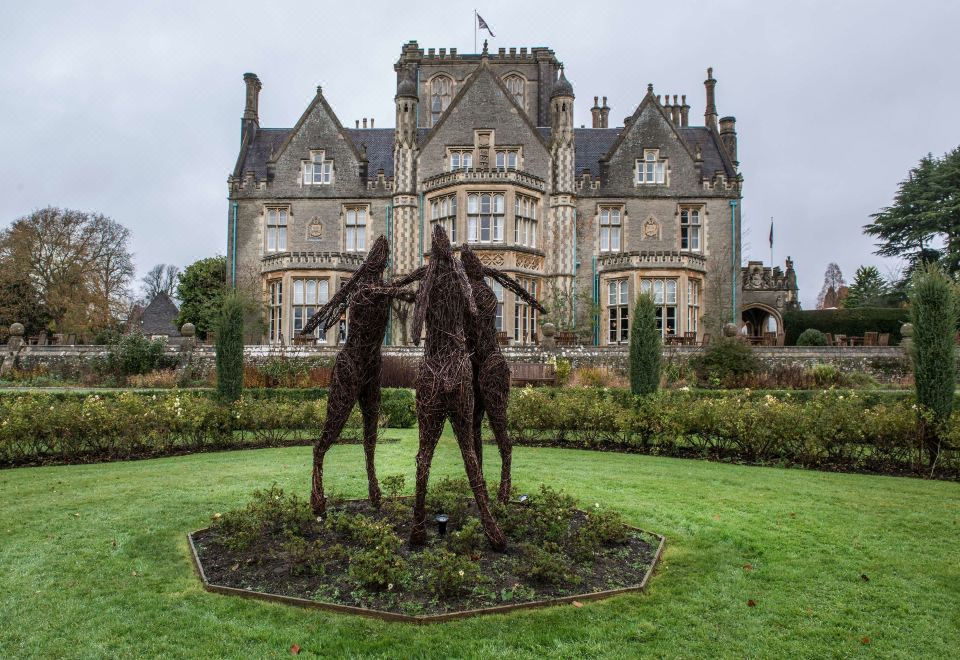 a large stone building with a garden and two sculptures in the front yard , creating a unique and eye - catching display at De Vere Tortworth Court
