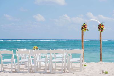 a beachfront wedding venue with rows of white chairs and tables set up on the sandy shore at Wyndham Reef Resort Grand Cayman