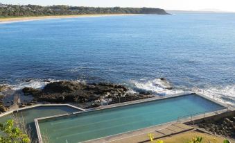 a large swimming pool surrounded by rocks , with a view of the ocean in the background at Beachfront Hallidays Point