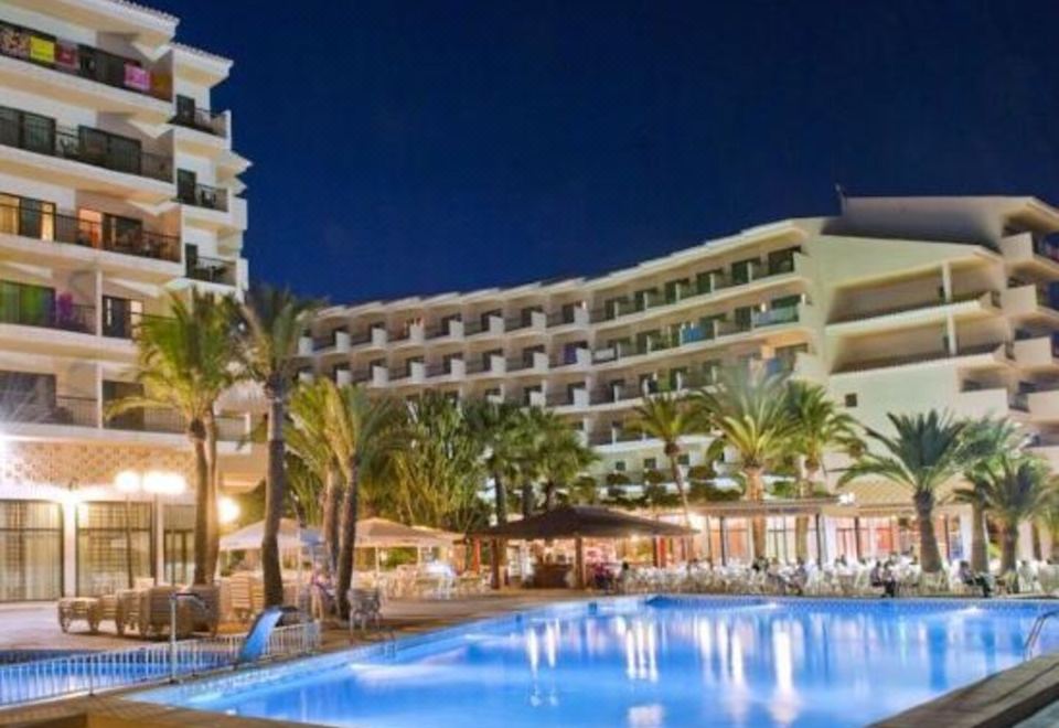 a large swimming pool is surrounded by palm trees and a hotel with multiple buildings at Hotel Cap Negret