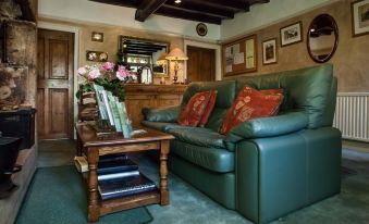 a cozy living room with a green leather couch , wooden coffee table , and a dining table at Ashfield House