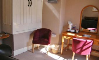 a room with a chair , table , and television is shown with sunlight streaming in from the window at The Kings Head Hotel