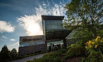 a modern building with a large glass facade , surrounded by trees and set against a blue sky at Sheraton Valley Forge King of Prussia