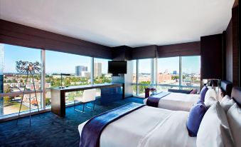 a modern hotel room with large windows offering a city view , two beds with white linens and blue accent pillows at W Atlanta – Downtown