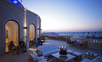 a rooftop patio with white couches , chairs , and tables set up for dining , overlooking the ocean at Mitsis Selection Laguna