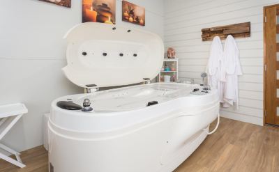 a white bathtub with a hot tub built into the wall , surrounded by white walls and a wooden floor at The Swan Valley Retreat