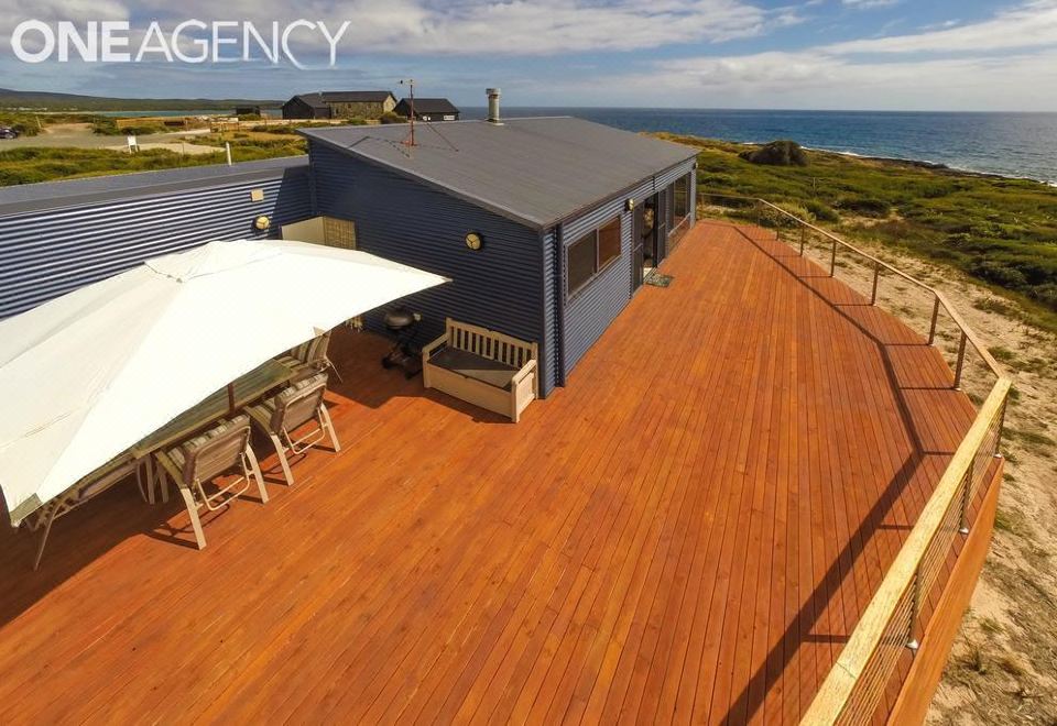 a rooftop deck with wooden flooring , umbrellas , and an umbrella stand , overlooking the ocean and sky at Seaspray