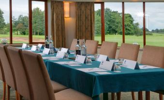 a conference room with a blue table covered in white paper and labeled name tags , surrounded by chairs and a view of a green field outside at Best Western Preston Garstang Country Hotel and Golf Club