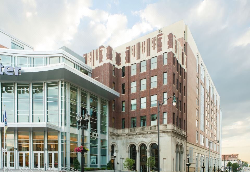 a modern office building with a red brick facade , surrounded by trees and benches , and situated on a bustling city street at Renaissance Allentown Hotel