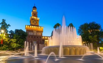 a large fountain in front of a building , with a clock tower in the background at Hotel Forum