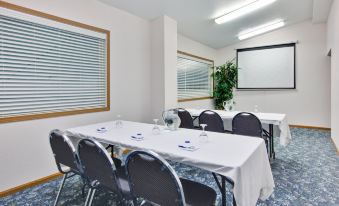 a conference room with white tables and chairs , a projector screen , and a potted plant at Holiday Inn Express Mackinaw City