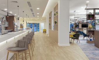 a modern restaurant with wooden floors , white walls , and gray bar stools near the dining area at Hampton by Hilton  Edinburgh Airport