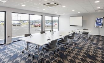 a conference room with a long table , chairs , and a projector screen is shown in the image at Hampton by Hilton Humberside Airport