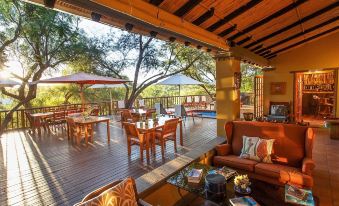 a spacious outdoor dining area with multiple tables and chairs , surrounded by trees and a wooden deck at Riverside Guest Lodge