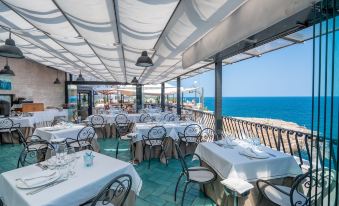 a restaurant with white tables and chairs , set against a backdrop of the ocean , under a clear blue sky at Covo dei Saraceni