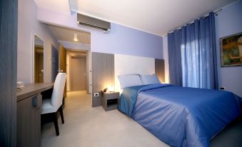 a modern bedroom with blue walls , white ceiling , and gray floor , featuring a bed , desk , and chair at Victoria Hotel