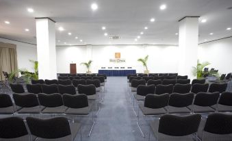 a large conference room with rows of black chairs arranged in a semicircle , facing a projector screen on the wall at Hotel Timor