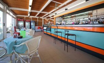 a modern restaurant with an open kitchen , blue and orange bar , and white tables and chairs at Hotel Caravel
