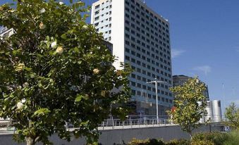 a tall white building with a blue sign is surrounded by trees and bushes in the city at Hotel Bahía de Vigo