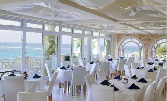 a large dining room with white tables and chairs , all set for a formal meal , overlooking the ocean at The Crane Resort