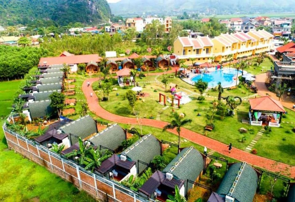 a resort with multiple buildings , a pool , and a playground surrounded by lush greenery and mountains at Doan Gia Resort Phong Nha