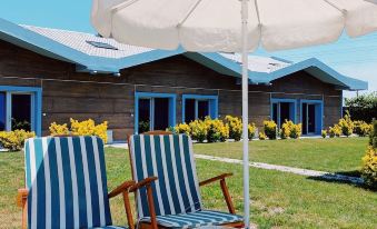 a row of blue and white chairs under a white umbrella in front of a row of brown wooden houses at La Vida Hotel