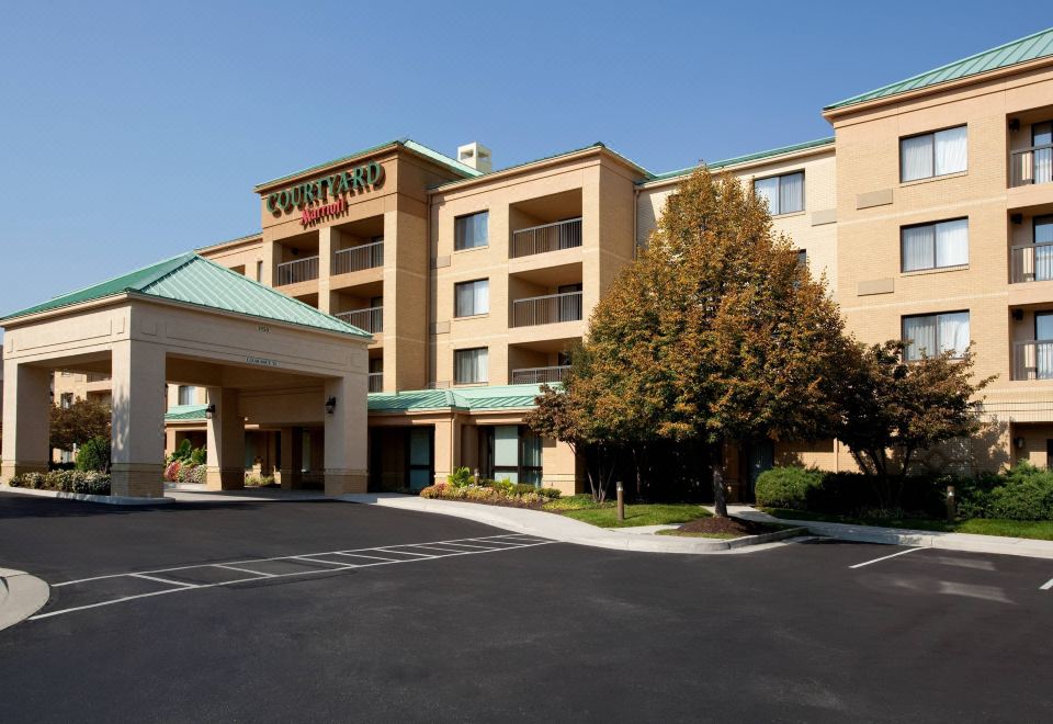 a large hotel building with multiple parking spaces and a large tree in the front at Courtyard Richmond Northwest/Short Pump