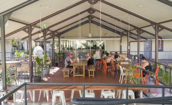 a group of people are sitting at tables in an open - air restaurant with wooden beams at YHA Byron Bay