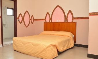 a bed with a wooden headboard and yellow sheets is in a room with pink walls at Hotel International