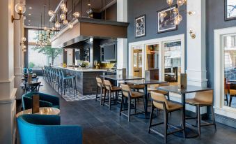 a modern restaurant with an open kitchen , bar area , and dining tables , decorated with blue chairs and pendant lights at Hilton Garden Inn Jackson Downtown