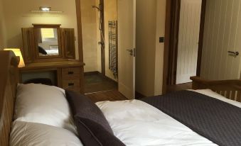 a bedroom with two beds , one of which is made up and the other has its sheets removed , along with a wooden desk and mirror at Shellow Lane Lodges