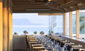 a long dining table set for a meal , with several chairs arranged around it , and a view of the ocean in the background at Aldemar Knossos Royal