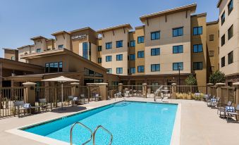 an outdoor swimming pool surrounded by a building , with several people enjoying their time in the pool at Residence Inn Riverside Moreno Valley