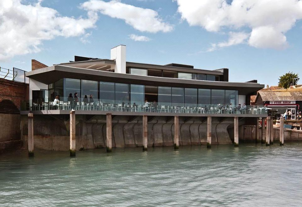 a modern building with a glass facade and a pier extending into the water , surrounded by people walking on the pier at Rocksalt