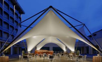 a large white tent is set up in a courtyard with tables and chairs underneath at Unahotels Expo Fiera Milano
