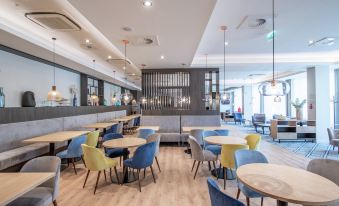 a modern restaurant with wooden tables and chairs , a bar area , and pendant lights hanging from the ceiling at Hampton by Hilton Oswiecim