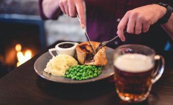a person is sitting at a dining table with a plate of food and a glass of beer at Black Bull Hotel