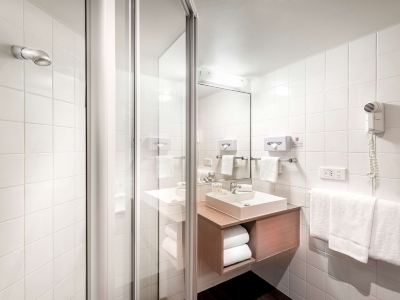 a modern bathroom with white walls , a glass shower enclosure , and a wooden sink cabinet at Ibis Melbourne Hotel and Apartments