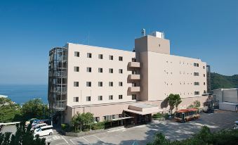 a large , beige - colored hotel building with many windows and balconies , situated in a city area surrounded by trees and cars at Kamenoi Hotel Atami Annex