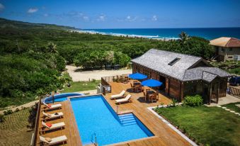 a large wooden house with a swimming pool and patio furniture is surrounded by greenery at Santosha Barbados