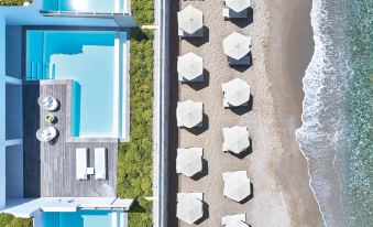a bird 's eye view of a beach with umbrellas , lounge chairs , and a pool in the foreground at Grecotel Lux.ME White Palace