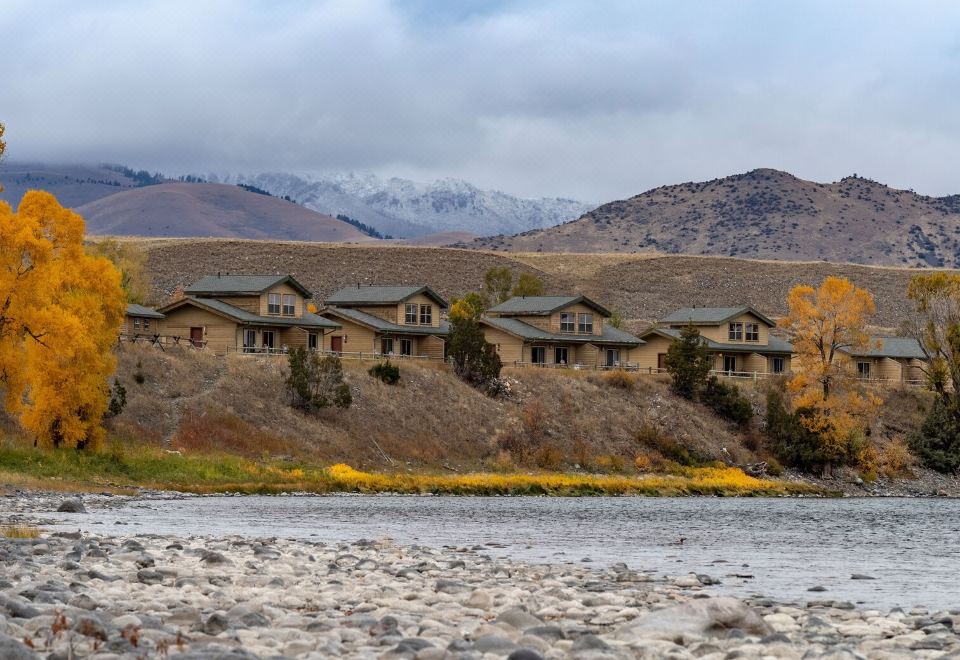 a group of houses built into the side of a hill next to a river , with mountains in the background at Yellowstone Valley Lodge, Ascend Hotel Collection