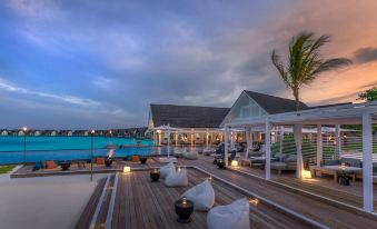a beachfront hotel with an open - air swimming pool , surrounded by lounge chairs and umbrellas , as the sun sets in the background at Four Seasons Resort Maldives at Landaa Giraavaru