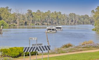 a boat is sailing on a river with trees in the background and a stop sign on the shore at Mildura Riverview Motel