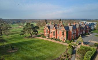 a large , red brick house with a green lawn and trees in the foreground , under a clear blue sky at Rockliffe Hall Hotel Golf & Spa
