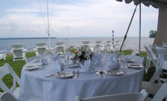 a beautifully set dining table with white tablecloths and blue chairs , set for a formal event on the shore at The North Hero House Inn & Restaurant