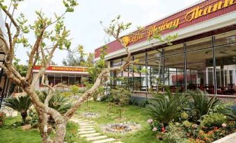 a restaurant with a large tree in front of it , surrounded by greenery and flowers at Hoang Trung Hotel